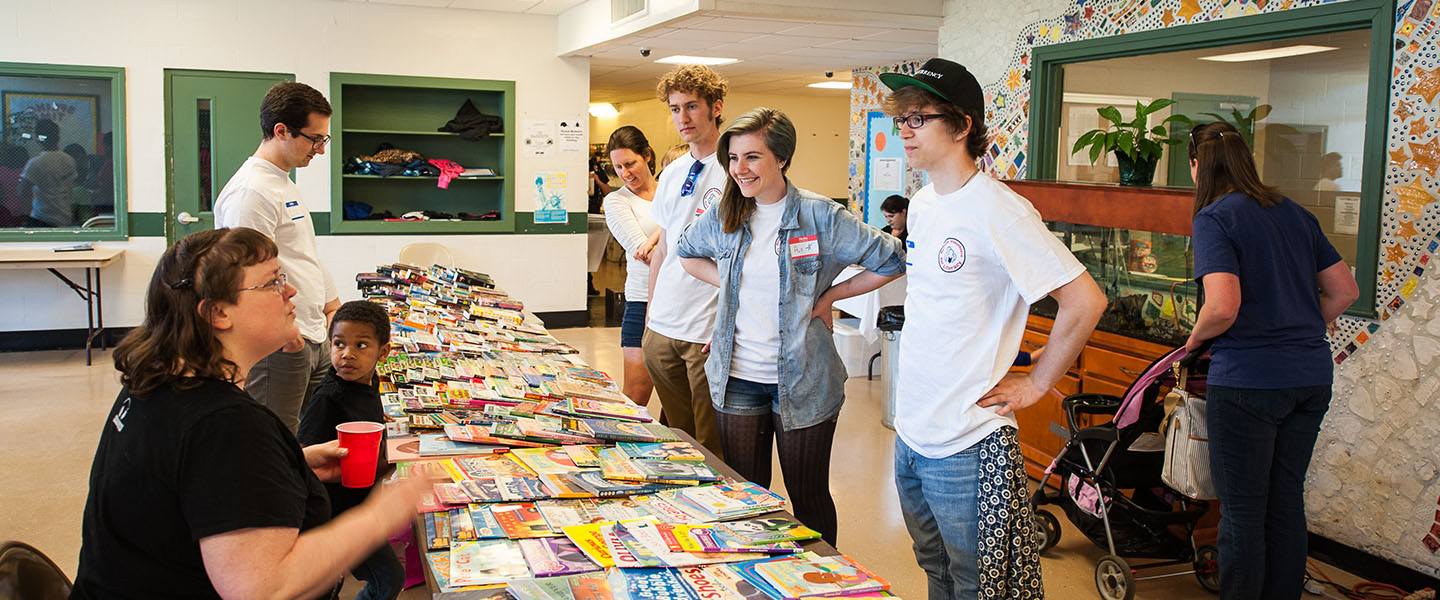 Students stand in front of a folding table set up with rows of children's books.