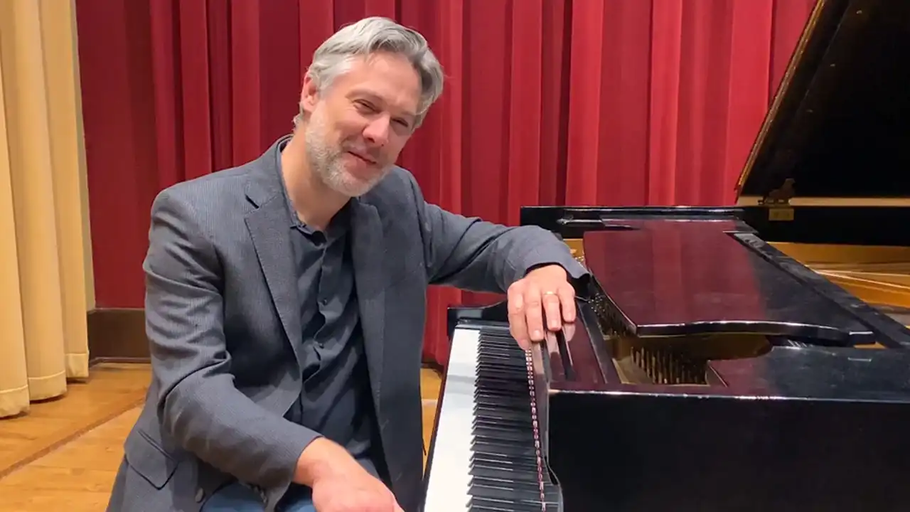 Professor Alex Graham talks at a piano about the Commercial Music Program
