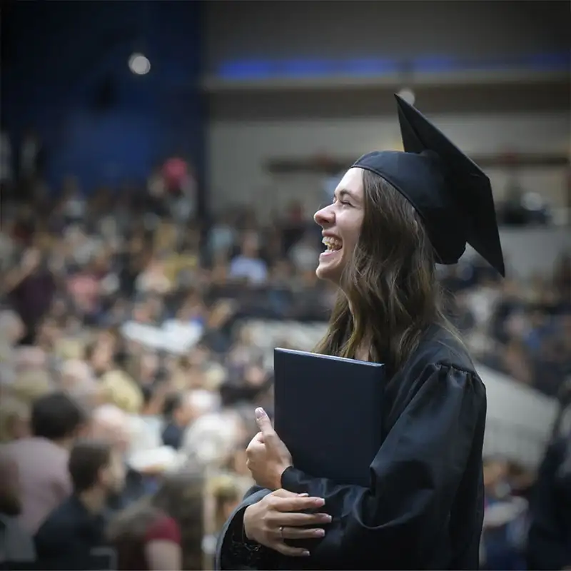 An image of a female student with cap and gown standing during commencement ceremony