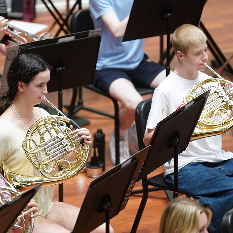 Students playing the french horn in a concert hall during music camp