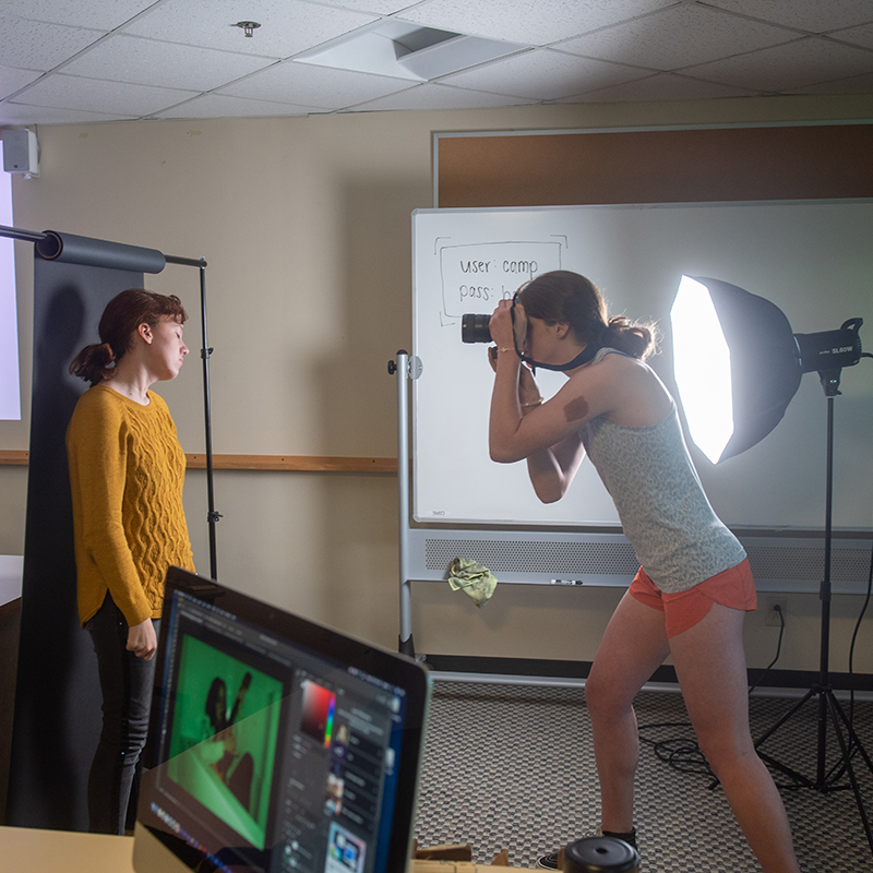One student taking a photographic portrait of another student using lighting equipment 