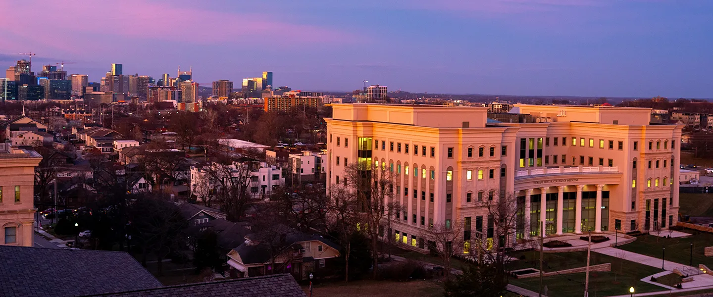 Panoramic view of the Frist College of Medicine building at sunset, with the Nashville city skyline in the distance and the sky illuminated in shades of pink and purple.