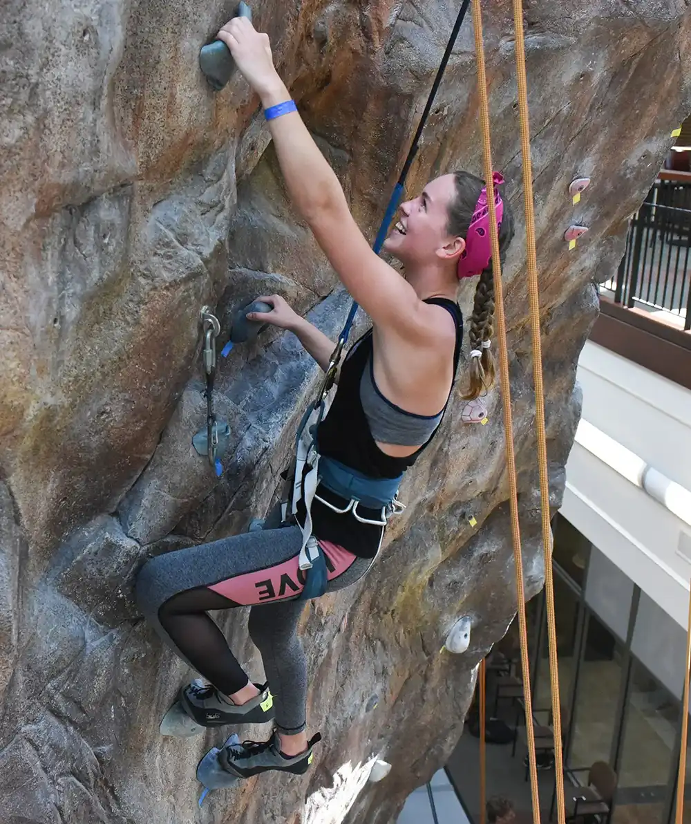 A student climbing the Beaman Rock wall with a smile