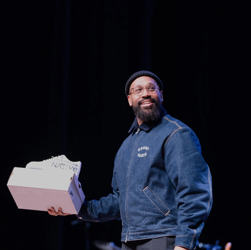 PJ Morton holding a shoe box in an auditorium