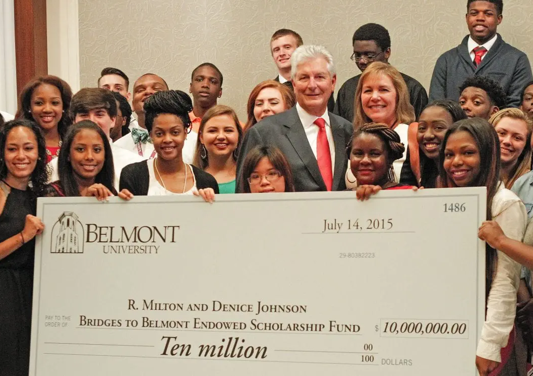 A large group of diverse students and supporters smile together while holding an oversized ceremonial check. The check, from Belmont University, is dated July 14, 2015, and made out to the “Bridges to Belmont Endowed Scholarship Fund” for $10 million. The check is presented by R. Milton and Denice Johnson, who stand near the center of the group.