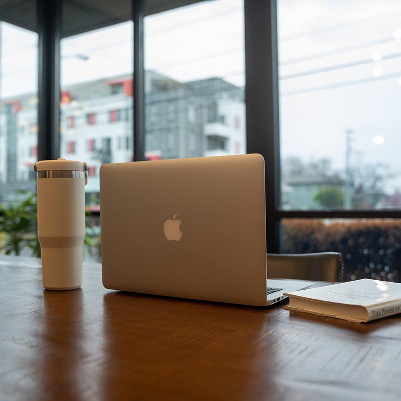 A laptop and a coffee on a table next to a window