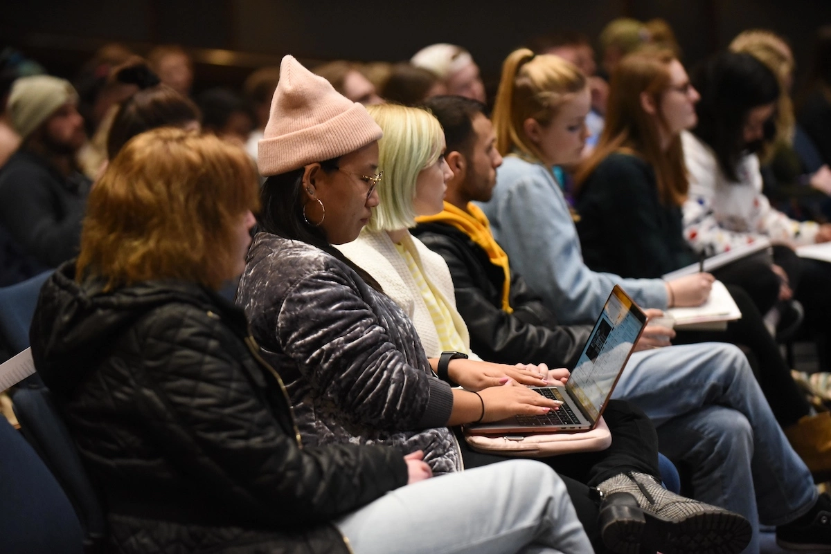 curb college students sitting in a row, listening to a presentation.