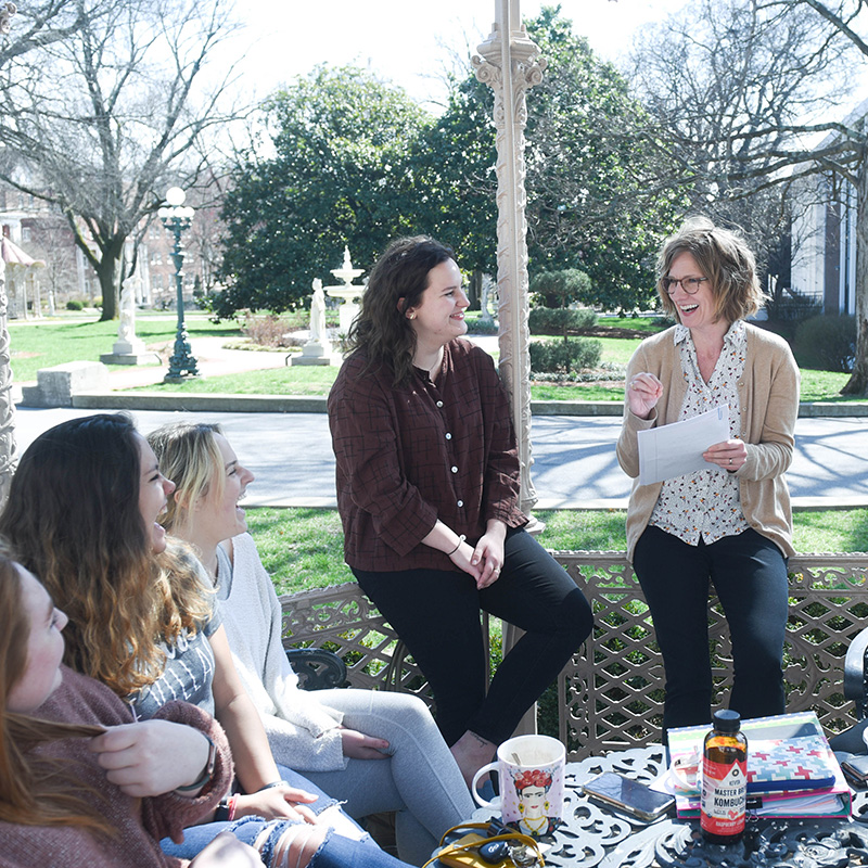 A group of Social Work students and a professor having a lively discussion outdoors on Belmont University's campus, sitting together in a gazebo.