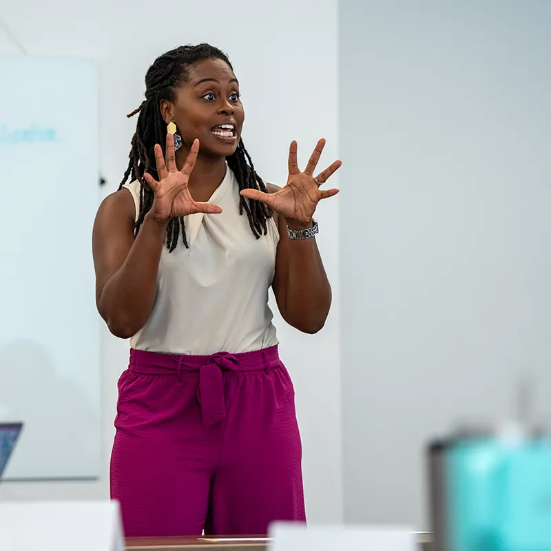 An enthusiastic instructor gestures expressively while teaching in a classroom, conveying passion and engagement.