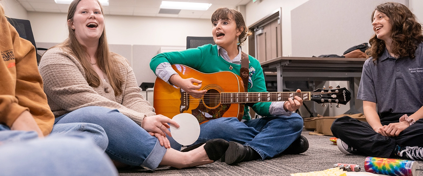 Students singing and playing instruments while seated on the floor.