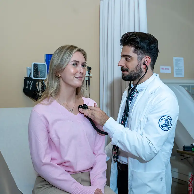 Nursing student holding a stethoscope to a patient's chest