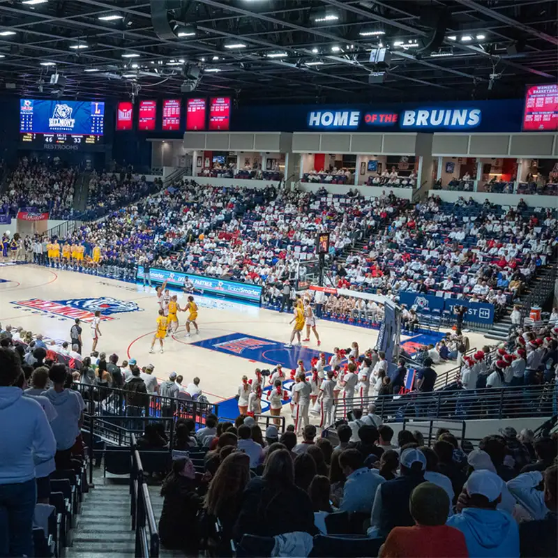 An indoor photo of Curb basketball arena during a basketball game with crowds of people in the stands and "Home of the Bruins" across the back wall