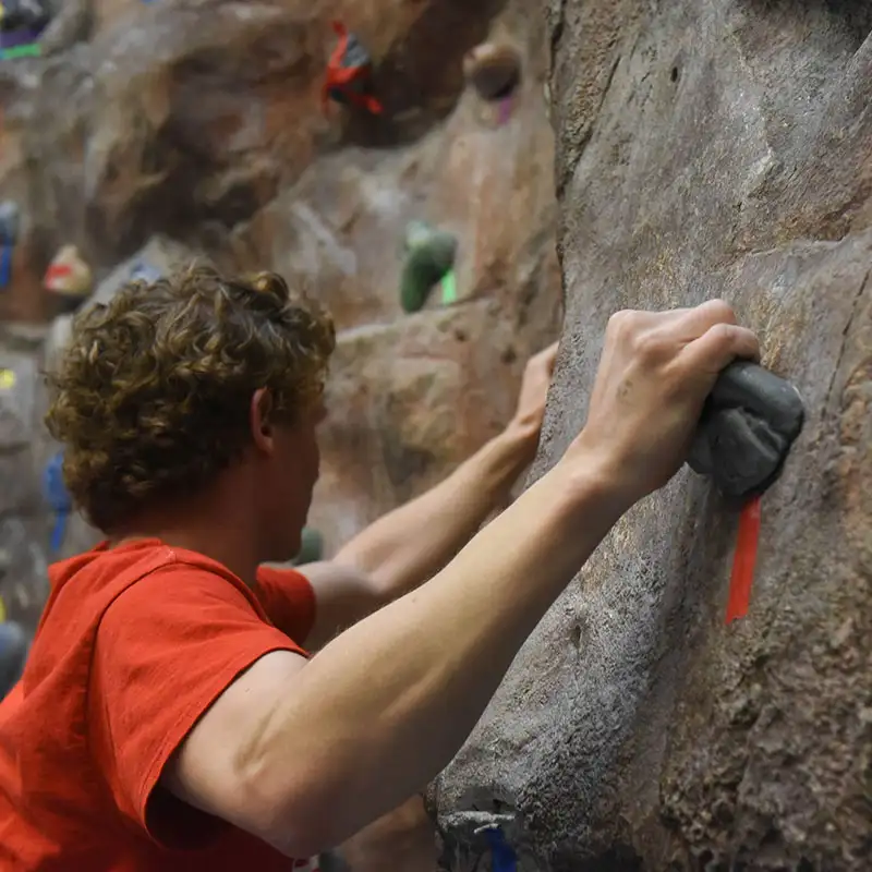 An indoor photo of a man gripping onto climbing wall 