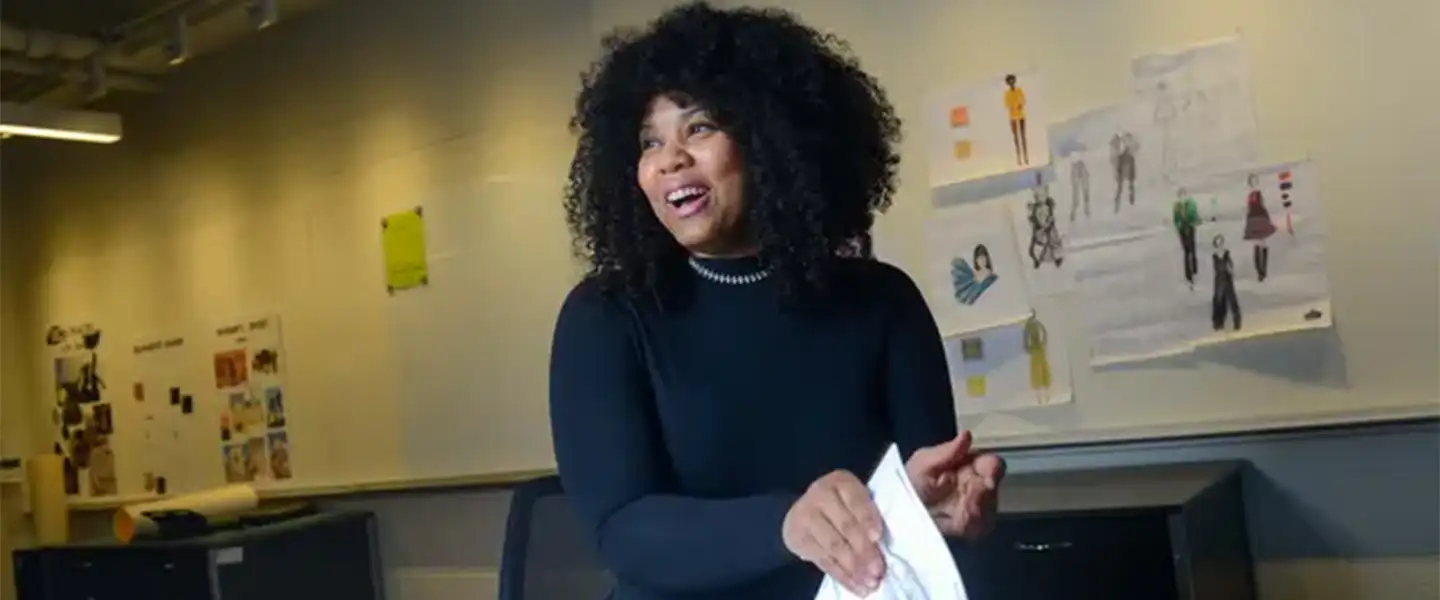 An indoor photo of a woman smiling and flipping through pages of fashion design sketches