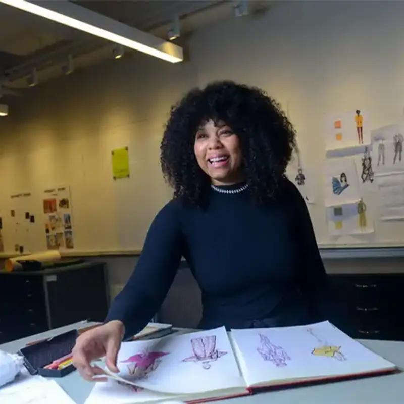 An indoor photo of an Adult Student turning through pages of a fashion design sketchbook