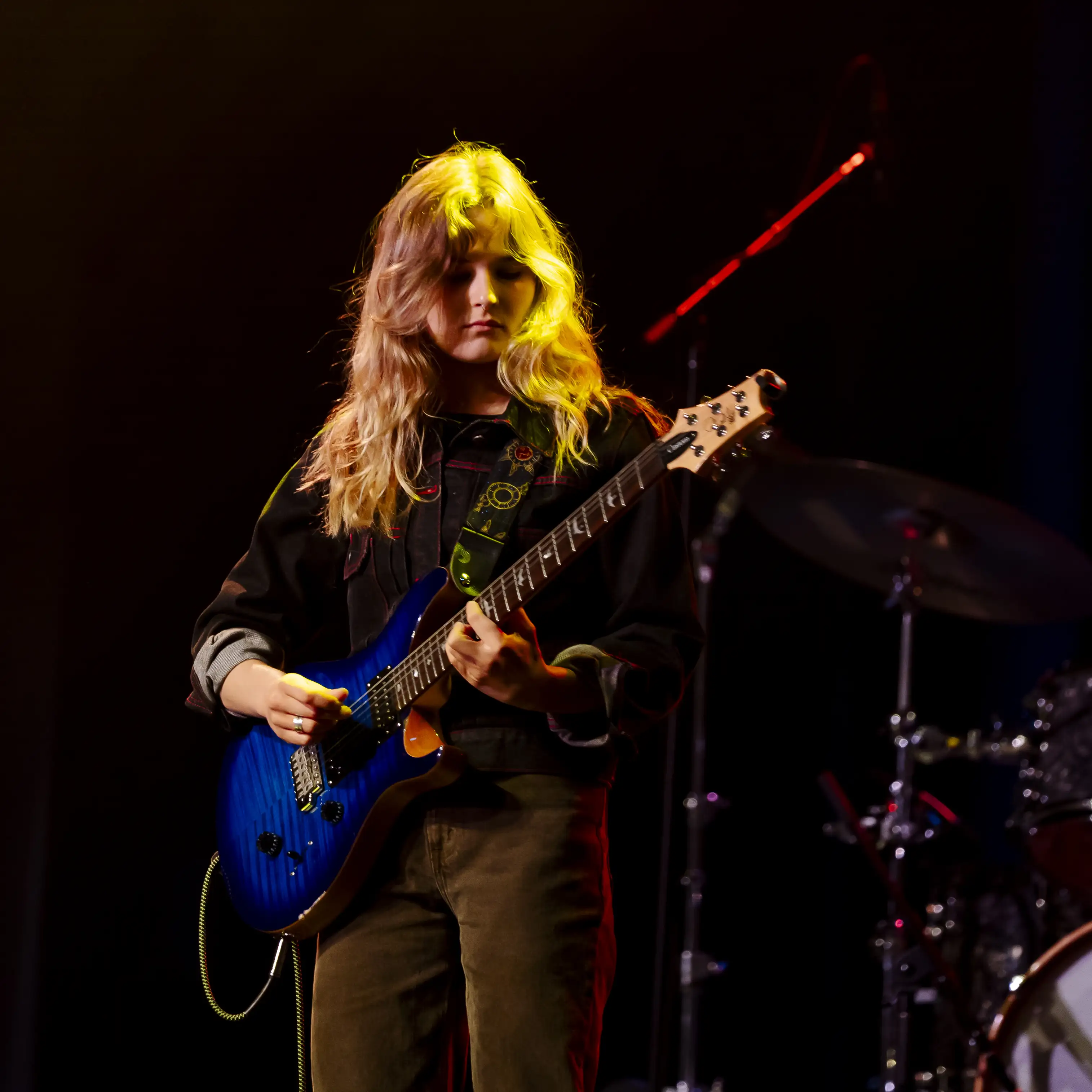 A Belmont University student plays electric guitar under stage lights during a live performance.