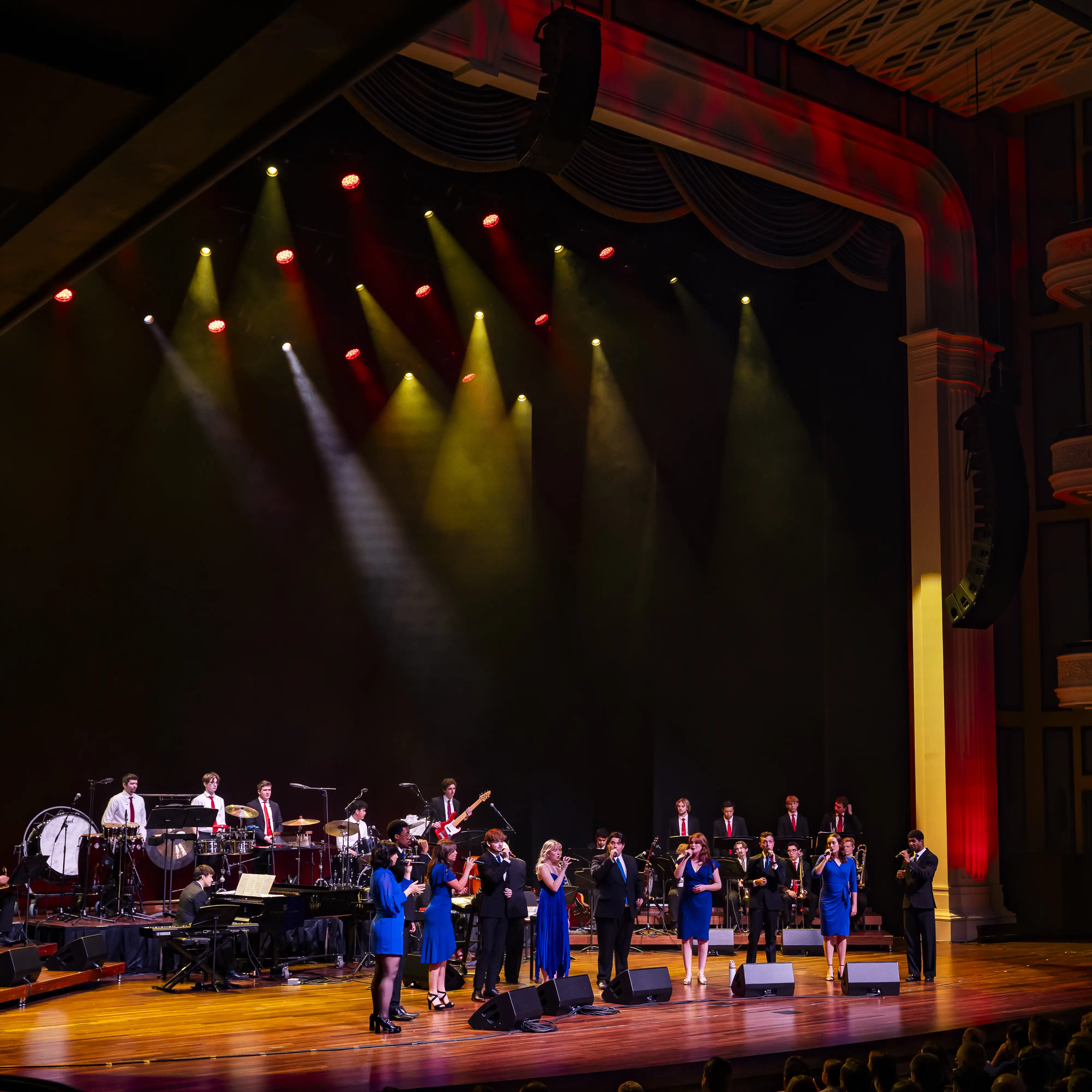 Belmont University students perform a full ensemble concert on stage, featuring vocalists, band members, and brass under theatrical lighting.
