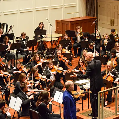 Belmont University orchestra performs under the direction of a conductor in a concert hall.