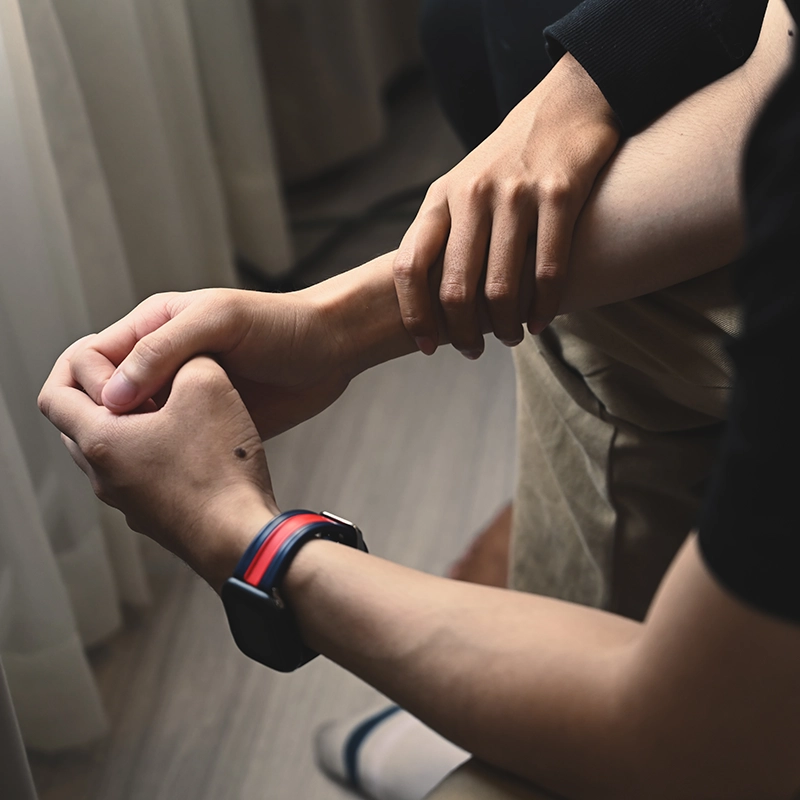 A close up of clasped hands with another set of hands placed on the persons arm in a comforting way