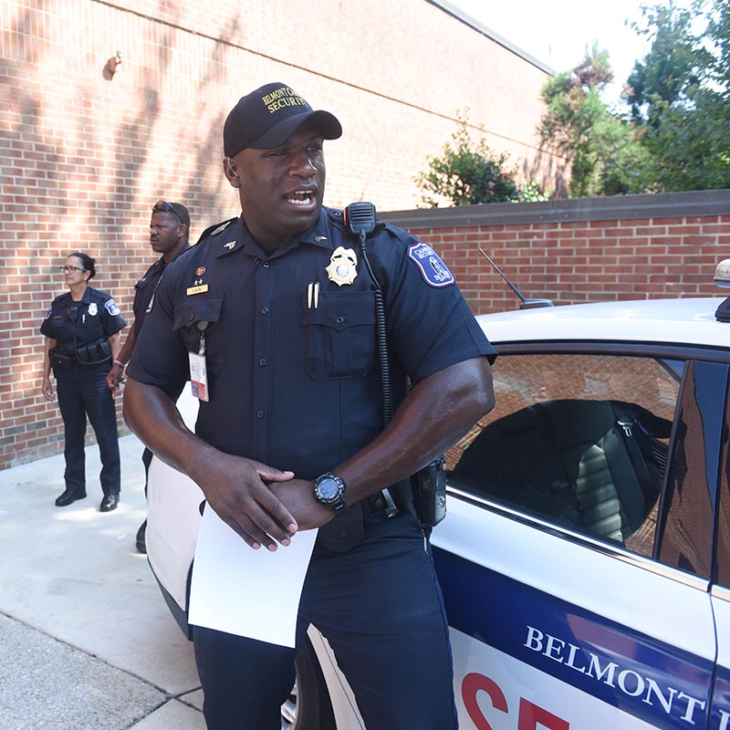 Belmont Security officer shouting assignments to other security officers outside by patrol car