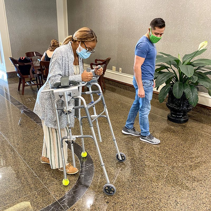 PT Student helping woman with walker navigate hallway 