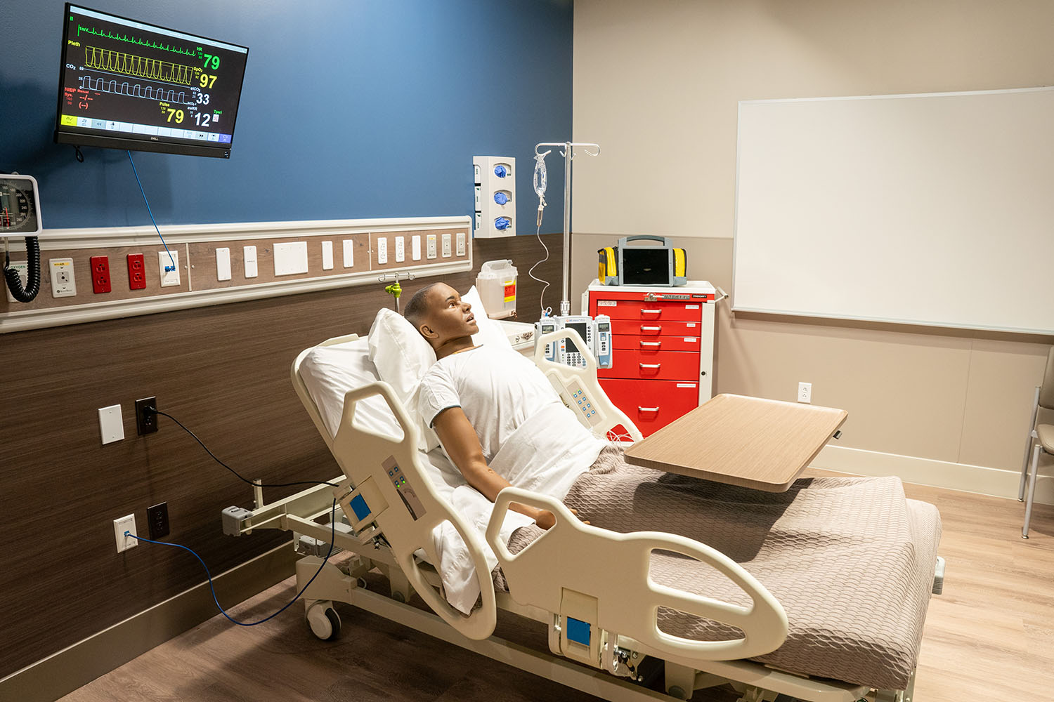 Close up of medical dummy in hospital bed with heart rate monitor and other training devices