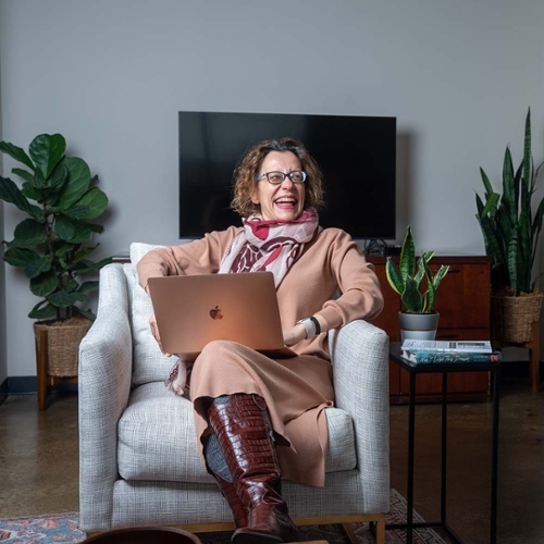 A woman sitting in a comfortable chair with a laptop in her lap laughing