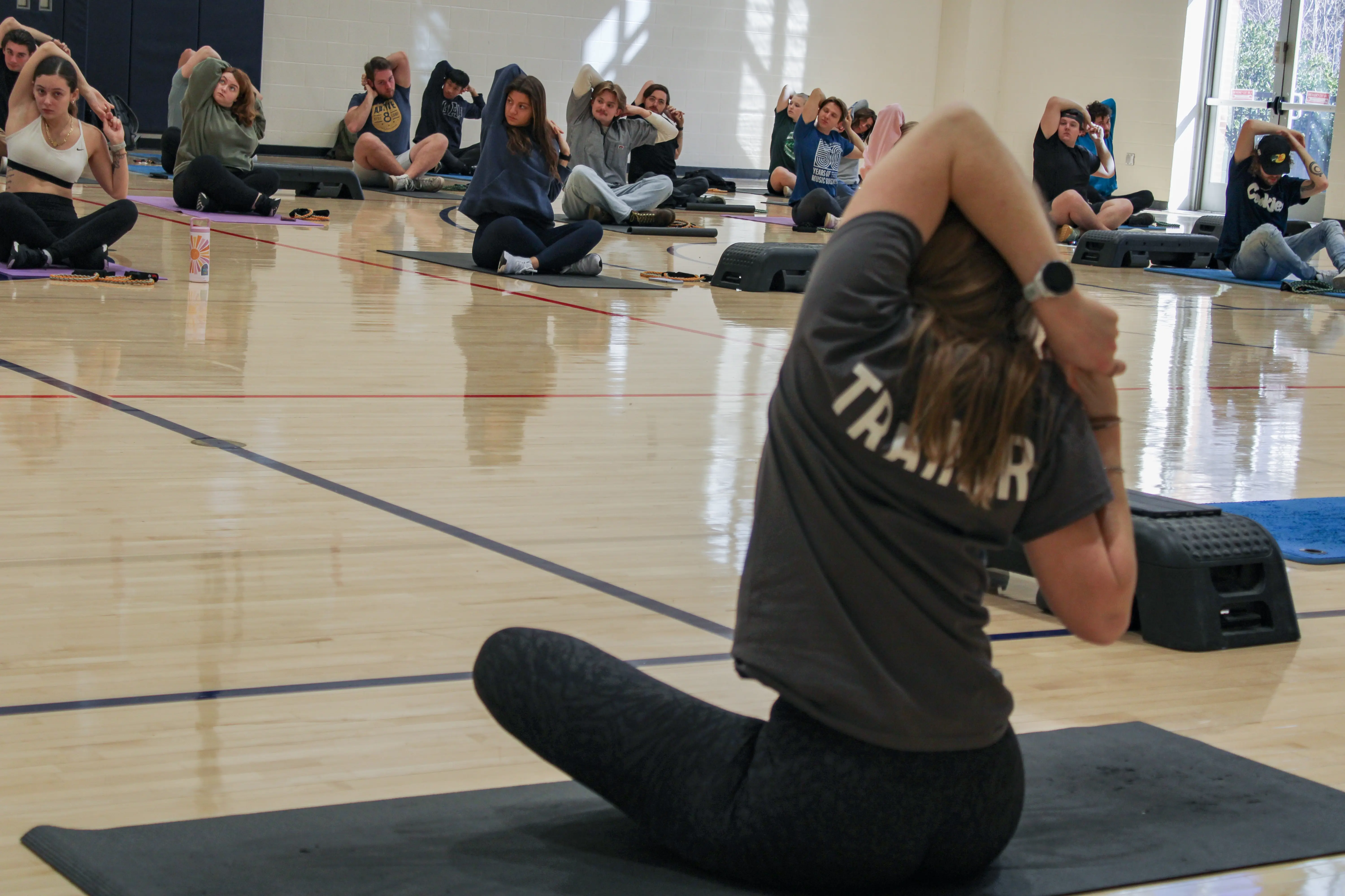 An indoor photo of a female student teacher leading a class through stretches