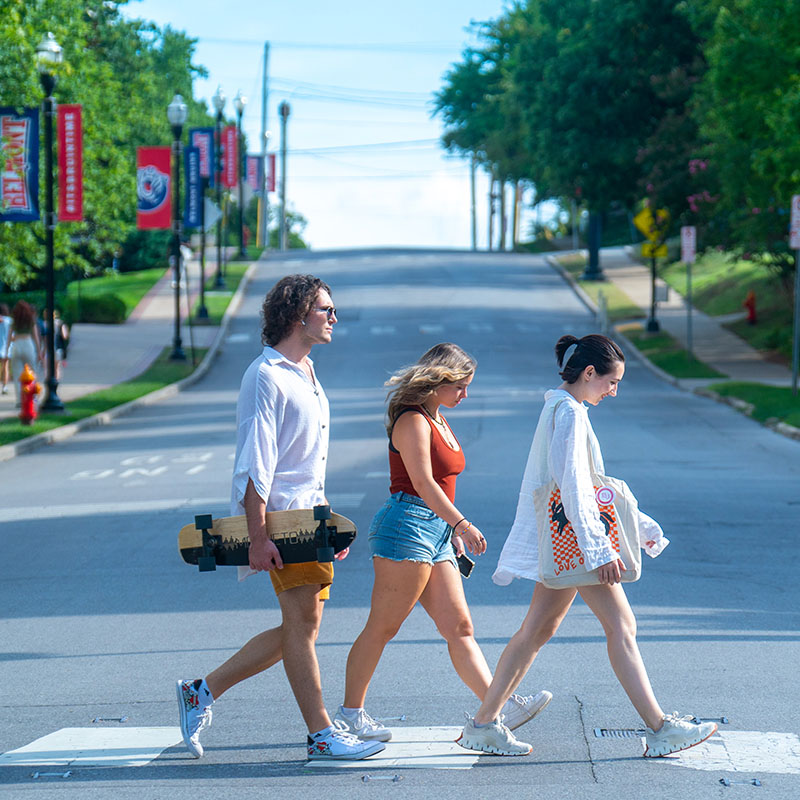 Three students walking across the road at a cross walk