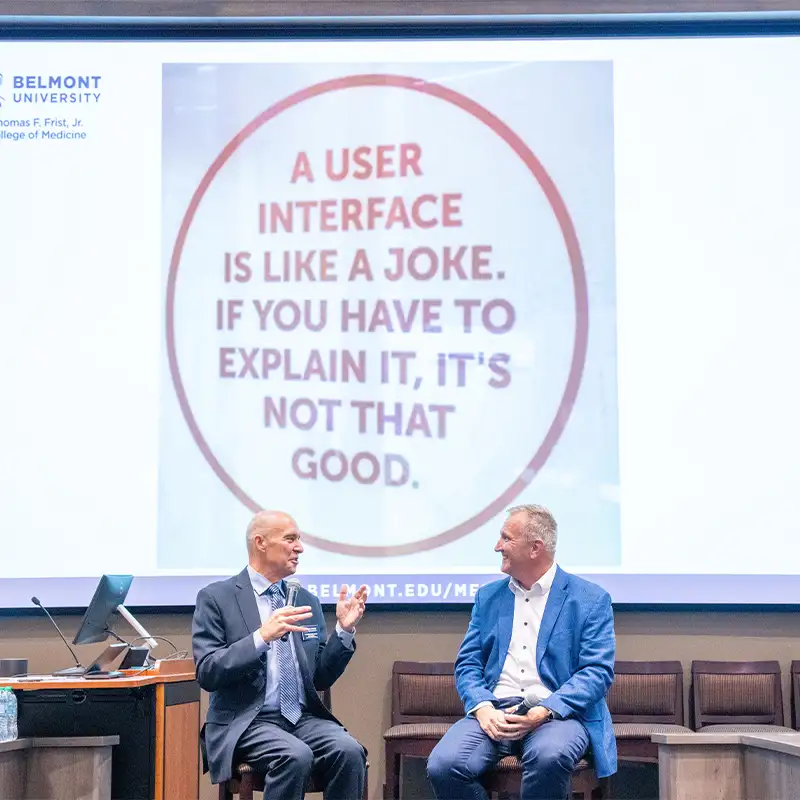 An indoor photo of two men seated and speaking at Symposium event