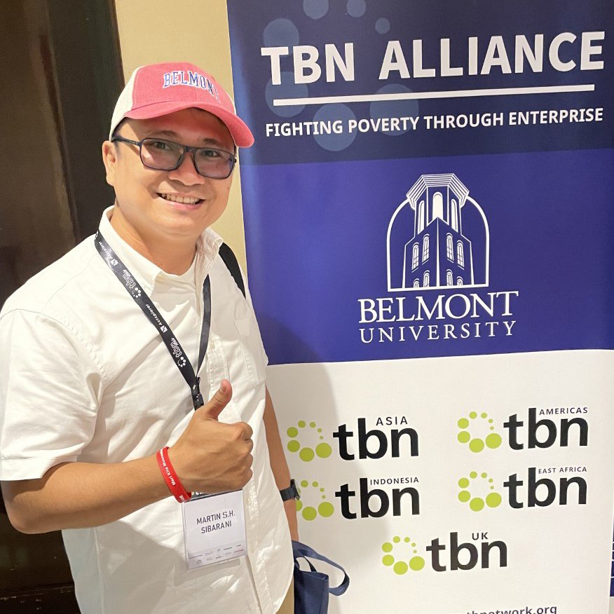 A man giving a thumbs up in front of a banner with the TBN and Belmont logo
