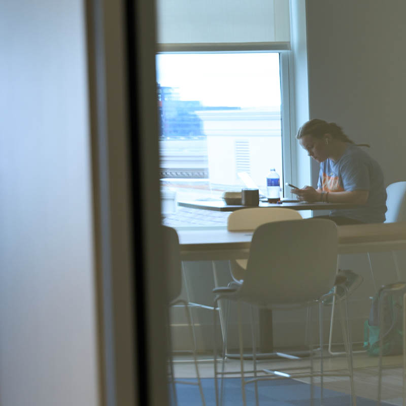 A reflection of a student in glass studying at a table wearing headphones