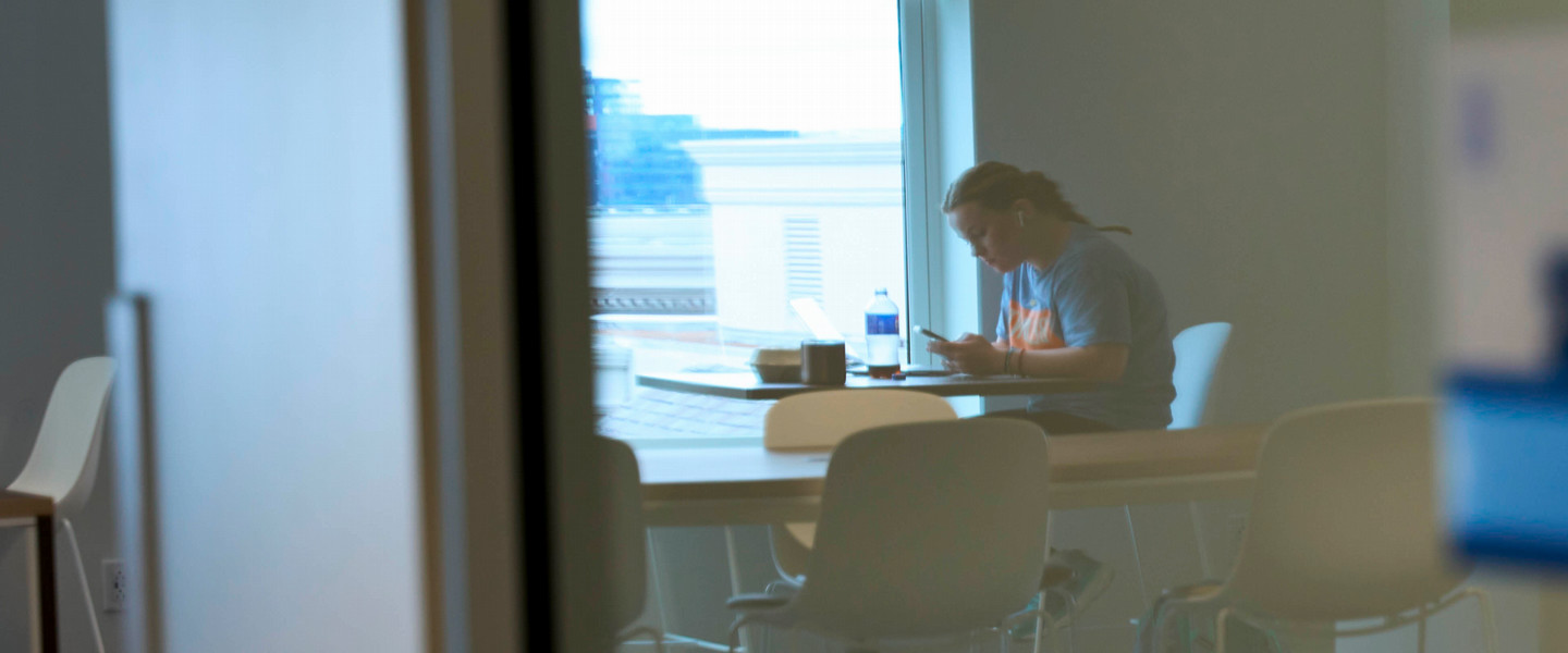 A reflection of a student in glass studying at a table wearing headphones