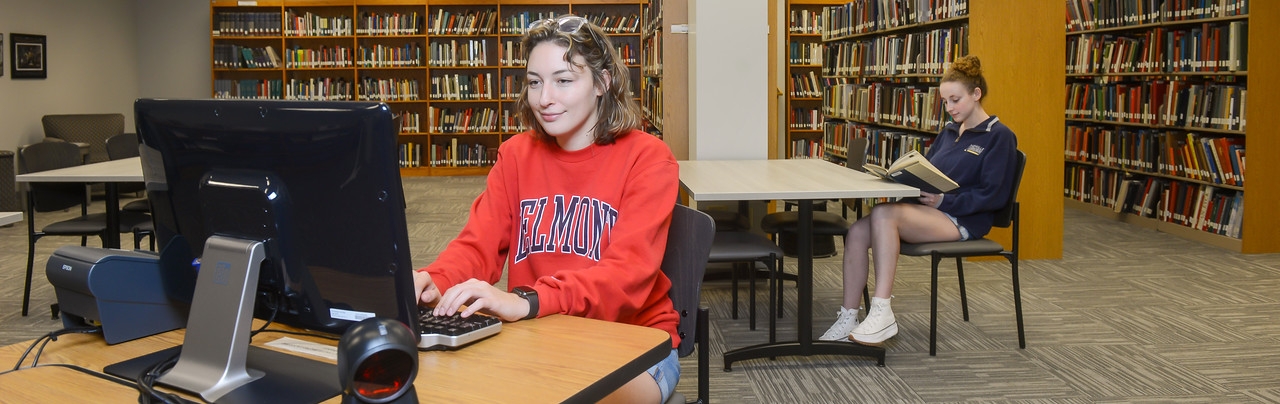Belmont students doing library research, both on a computer and with a book.
