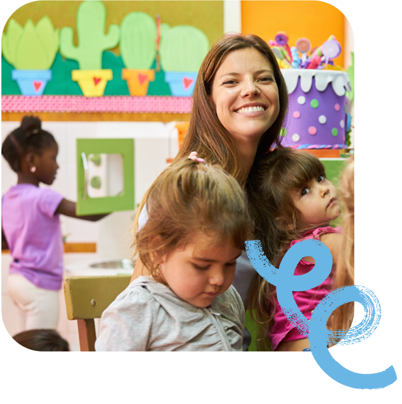 A preschool teacher with their students smiles at the camera