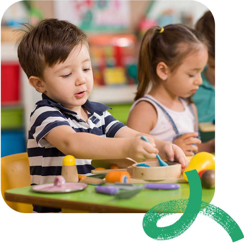 A preschool boy playing with clay in his classroom with other students