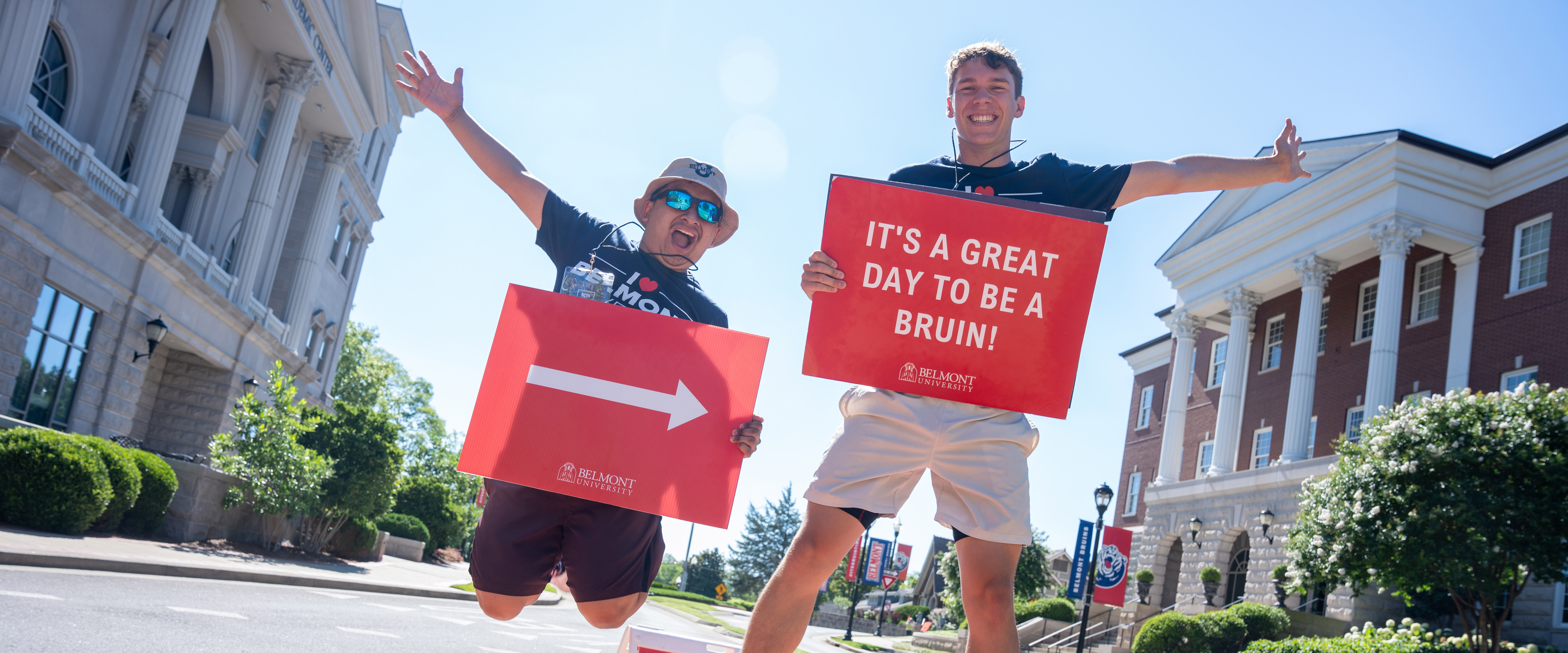 2 Orientation leaders jumping in the air with signs welcoming new students to belmont