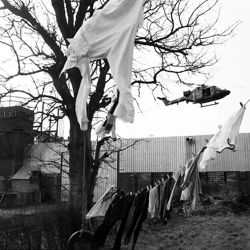 An outdoor photo of a helicopter flying over a building with clothesline in the foreground in Belfast