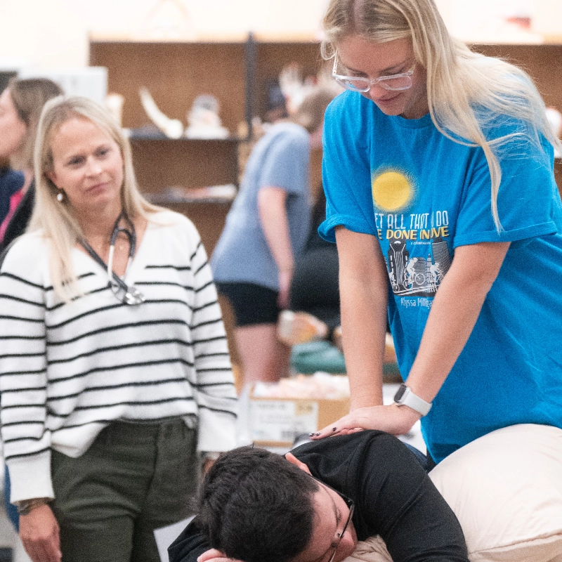 Healthcare student performs a hands-on medical procedure under an instructor's supervision.