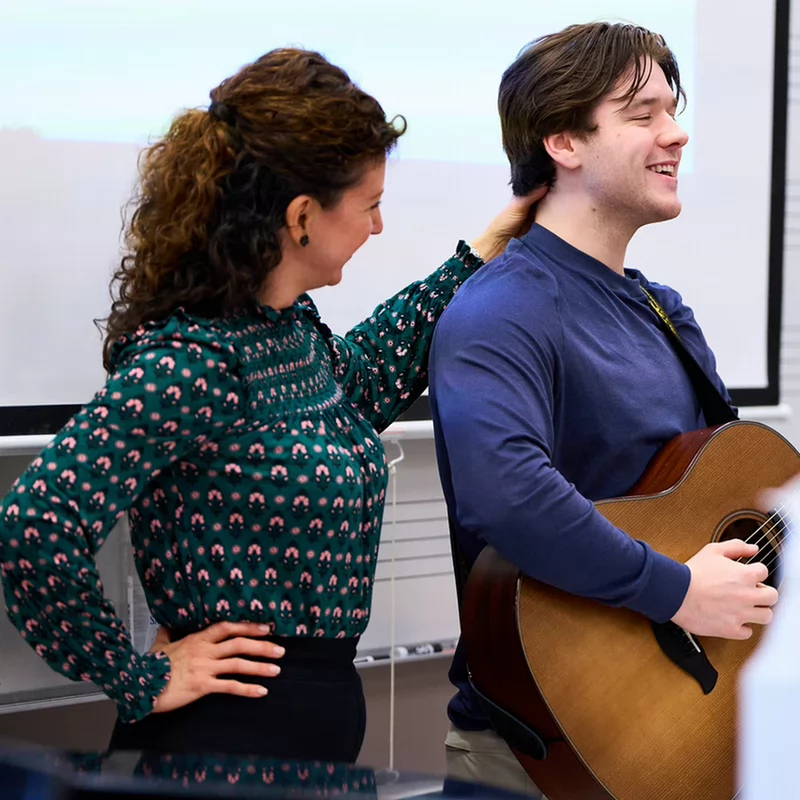 Lindsay Ison (PT) asists with posture of a student playing guitar and singing. 
