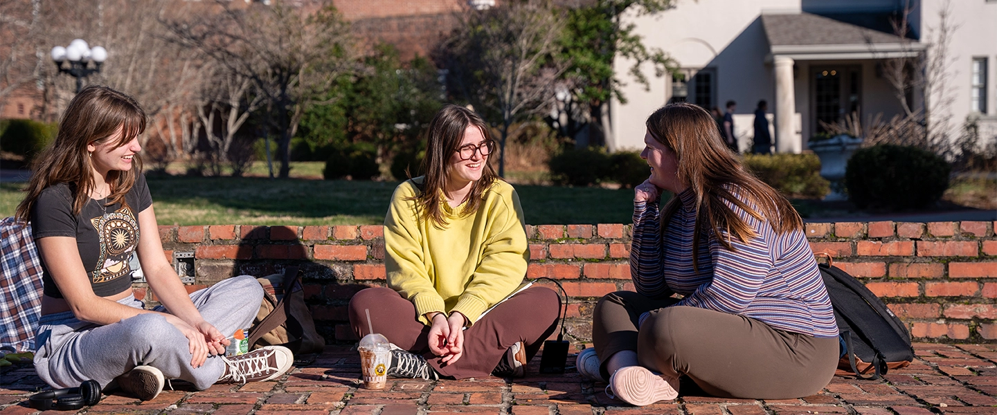 A small group of people outside seated on the ground in a semi-circle