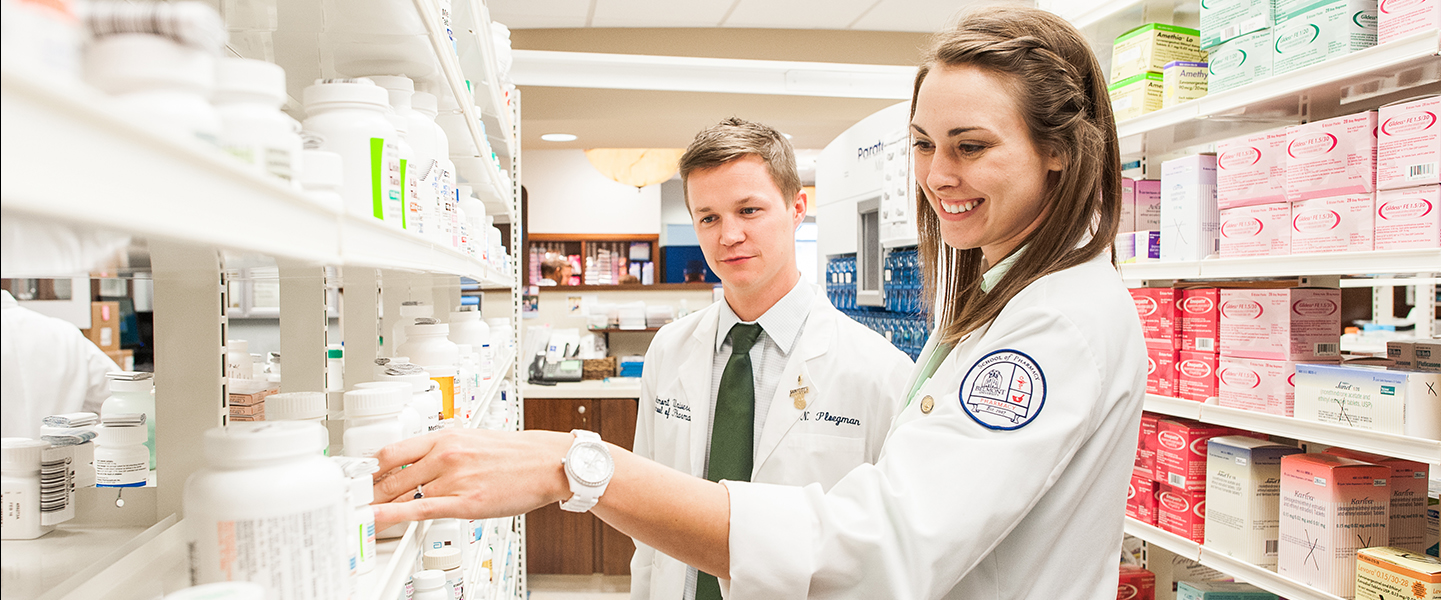 Two students in lab coats working in a pharmacy