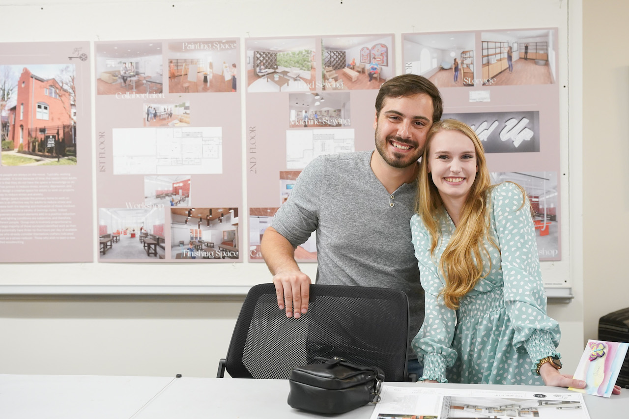 Two students standing next to each other in front of interior design work