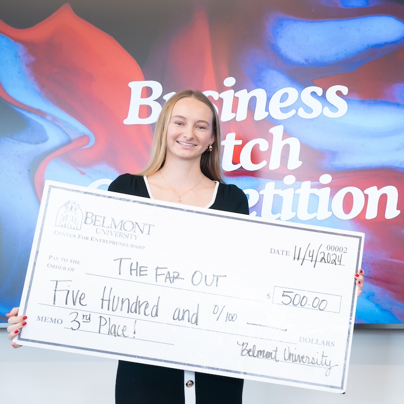 female student holding a giant check worth $500 made out to her company The Far Out