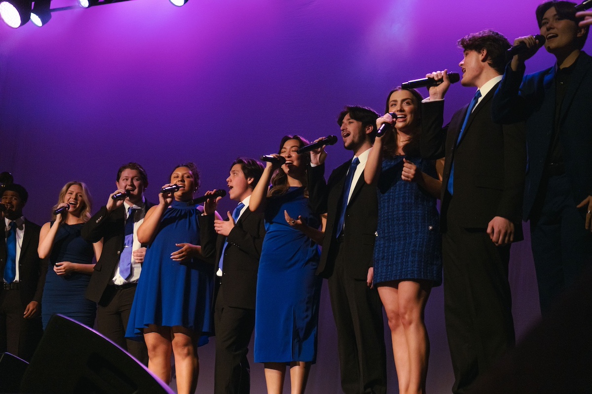 vocal ensemble in black and royal blue singing on stage