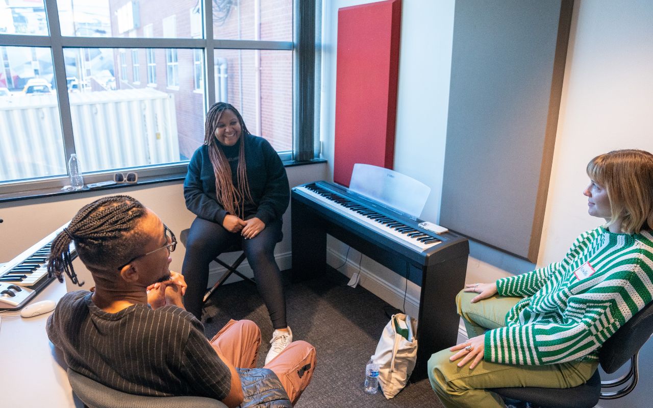 Three songwriters sit in a circle