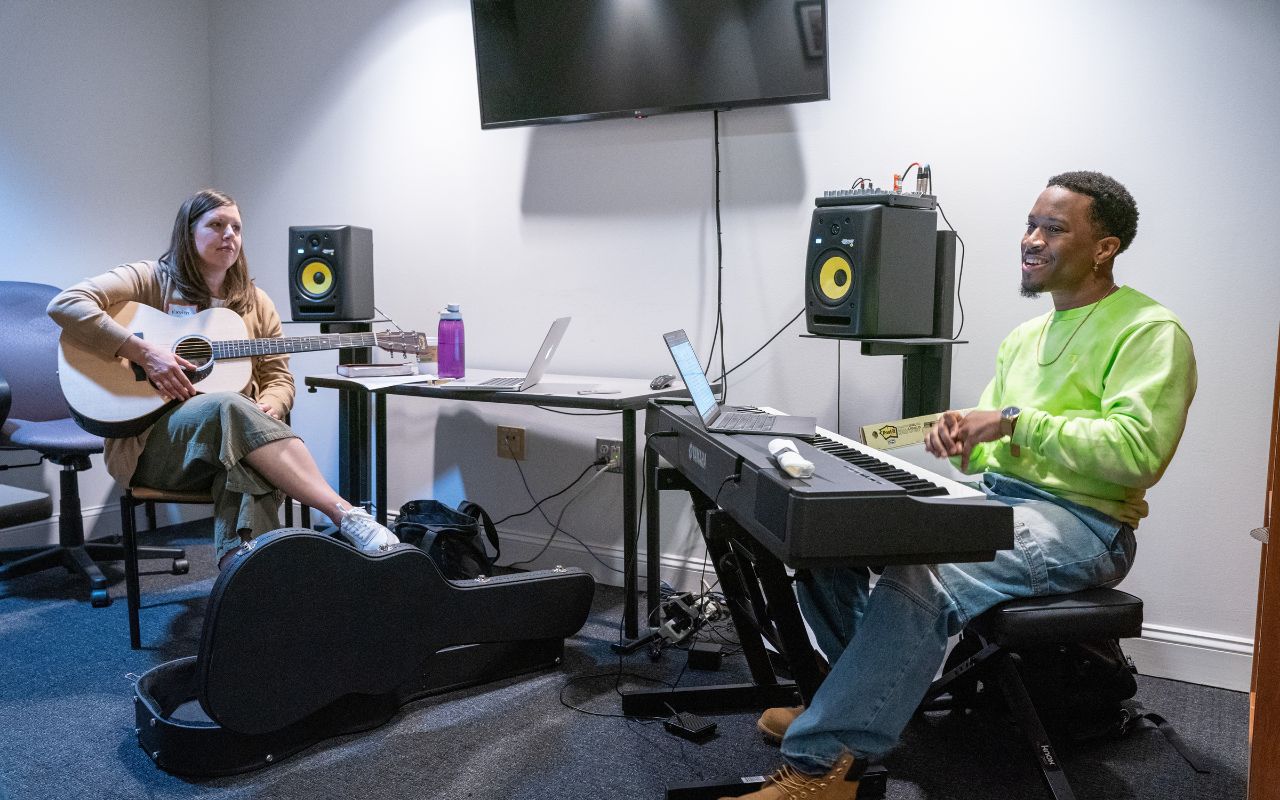 Woman sits with guitar and man sits behind keyboard