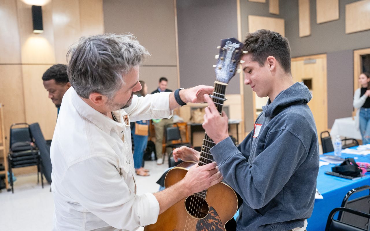 Man hands a younger boy a guitar