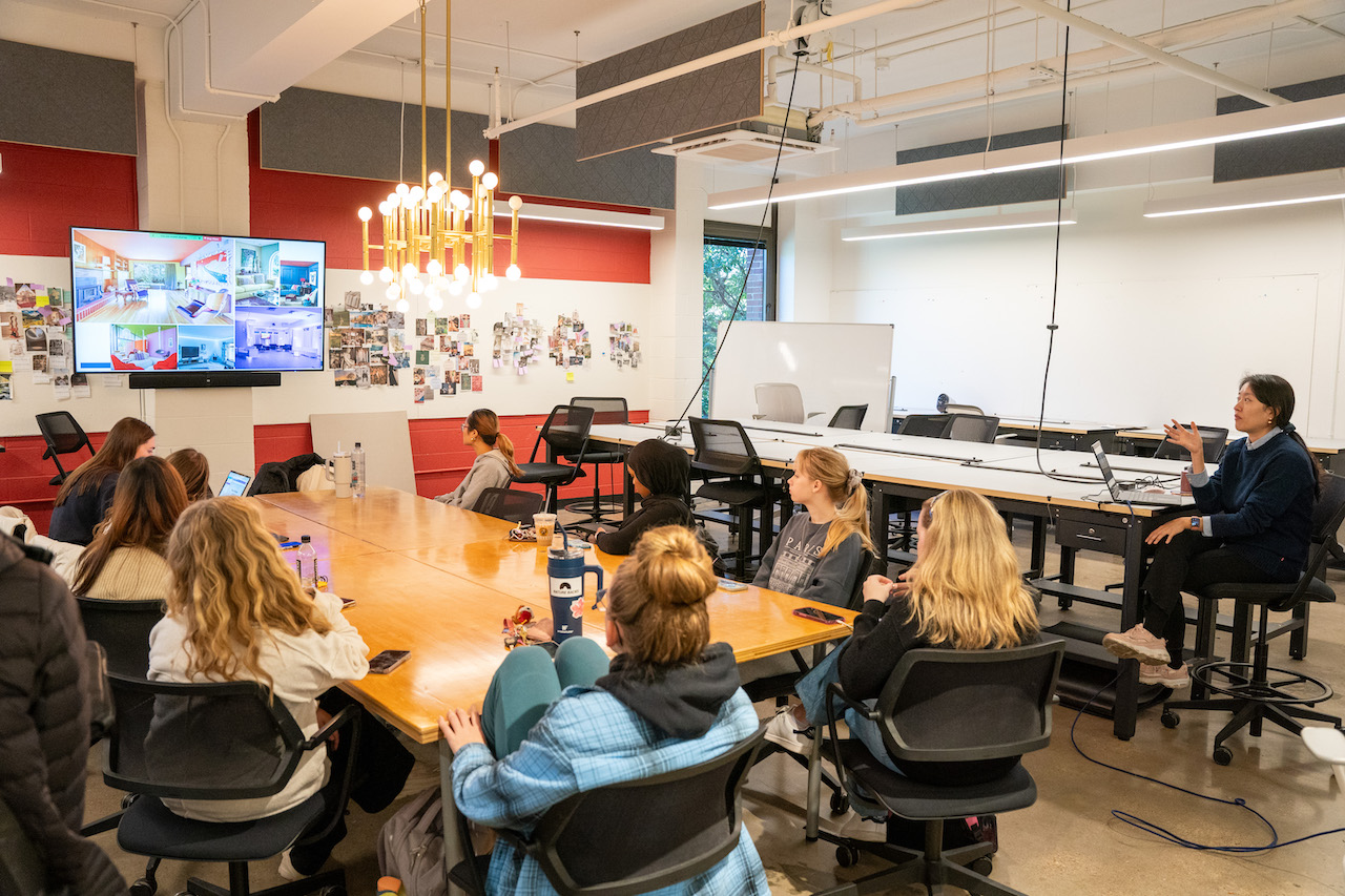 Interior design students sit around a table and critique a student's work