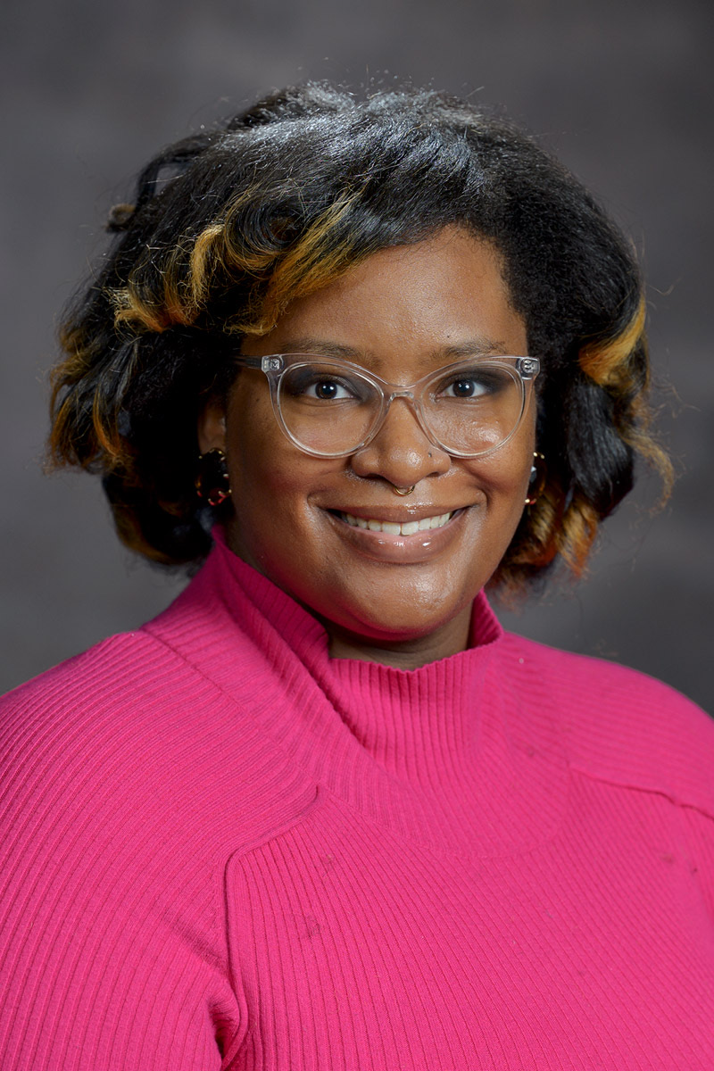 Headshot of Nia Allen, wearing a bright pink shirt and clear glasses